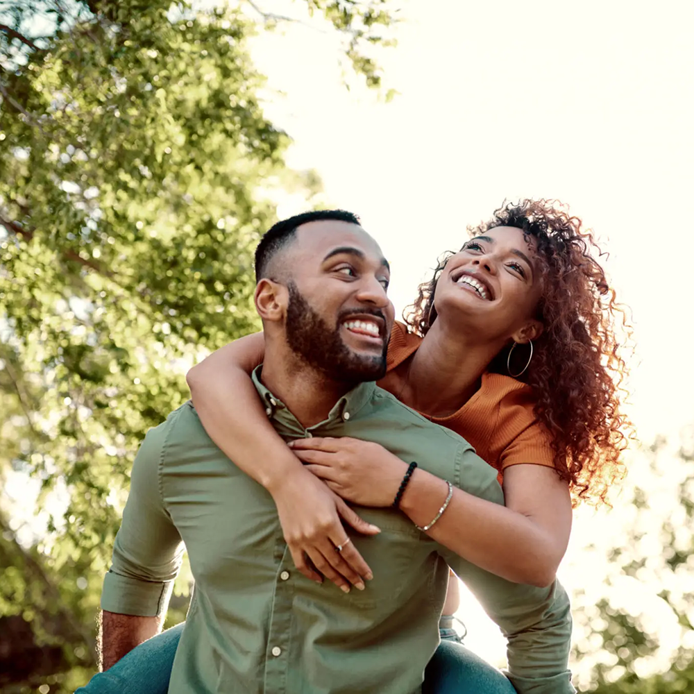 Couple enjoying a joyful piggyback ride outdoors in sunlight.