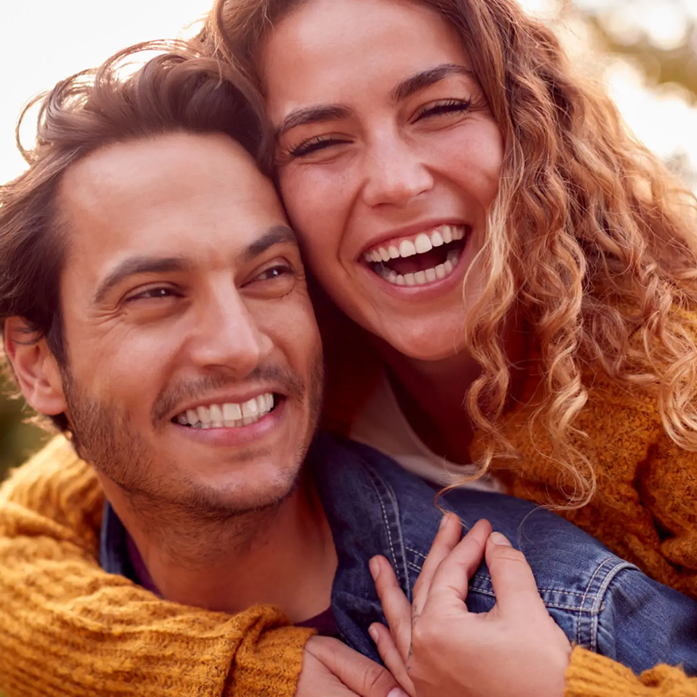 Smiling couple embracing outdoors, radiating happiness and warmth.