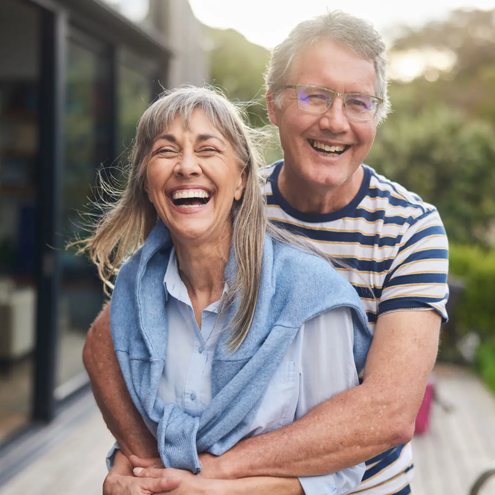 Elderly couple laughing and embracing outdoors in warm sunlight.