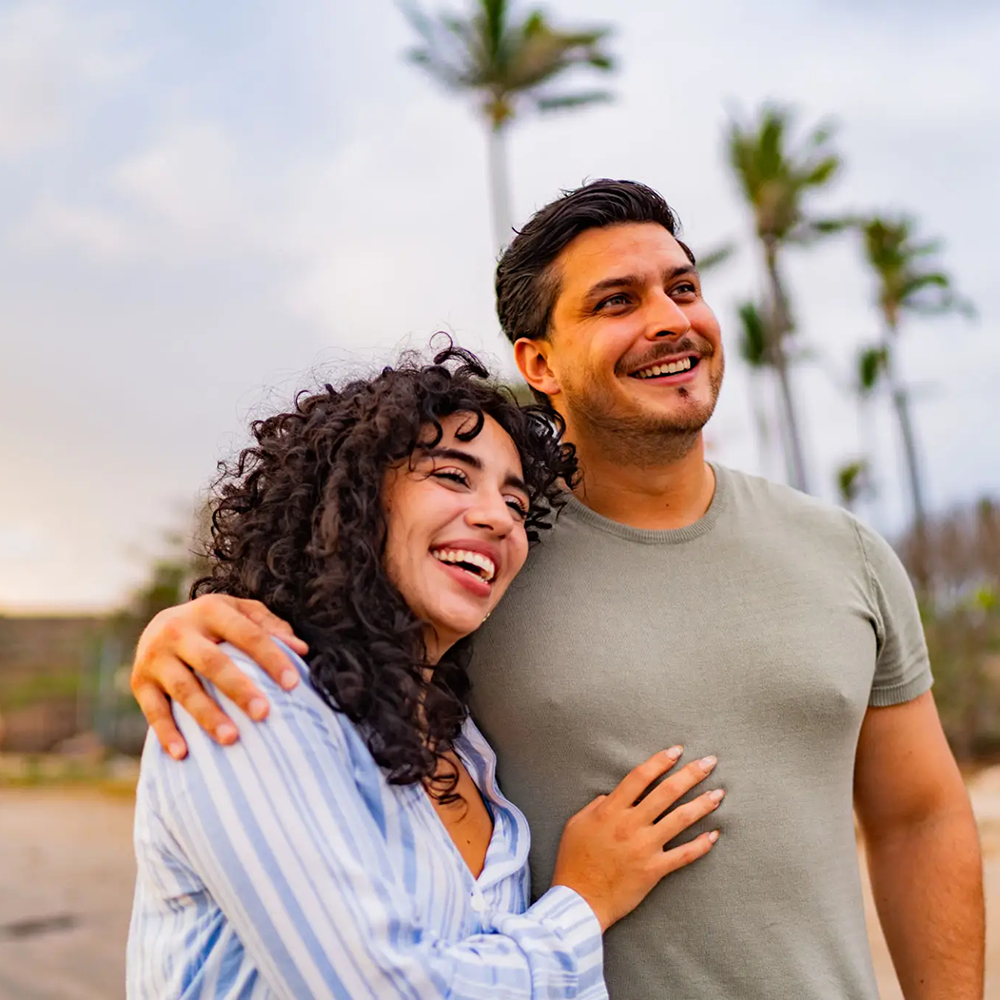 Happy couple enjoying a moment outdoors with palm trees in the background.
