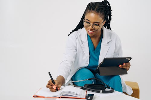 A smiling healthcare professional writing notes while holding a tablet.