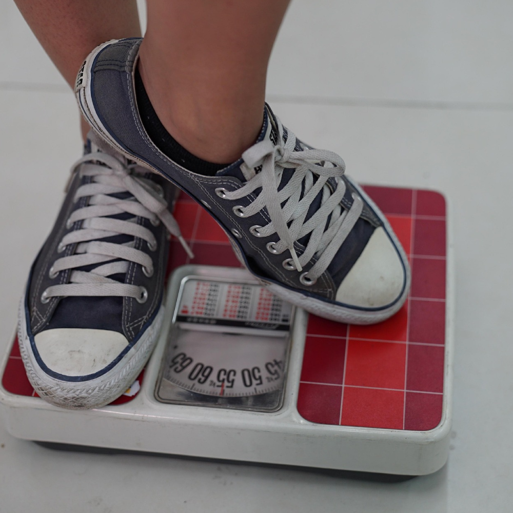 Person standing on a scale wearing black and white sneakers.