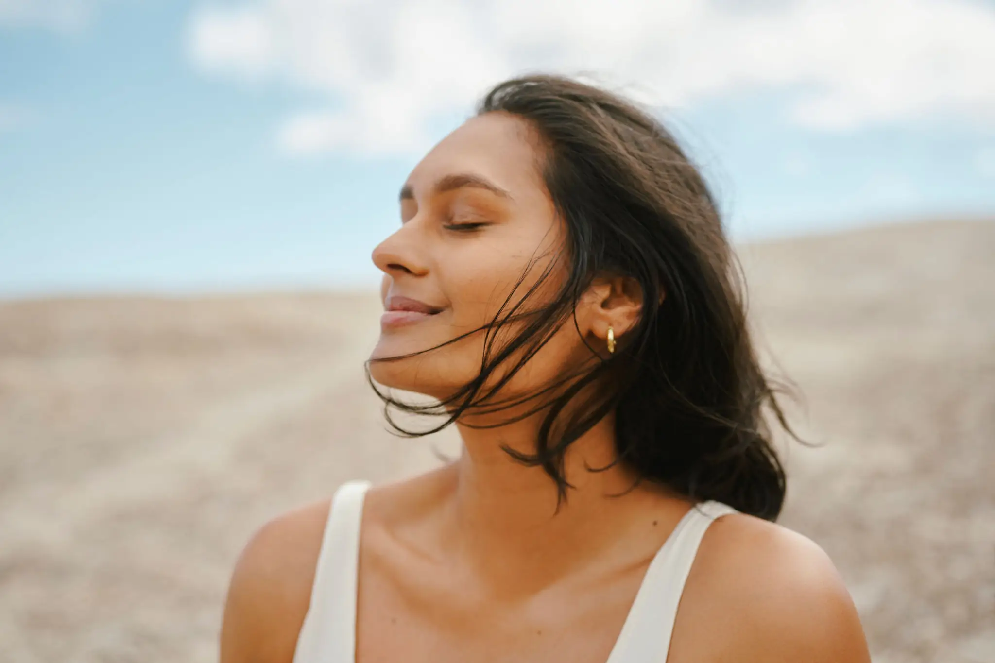 A woman with closed eyes enjoying a gentle breeze outdoors.