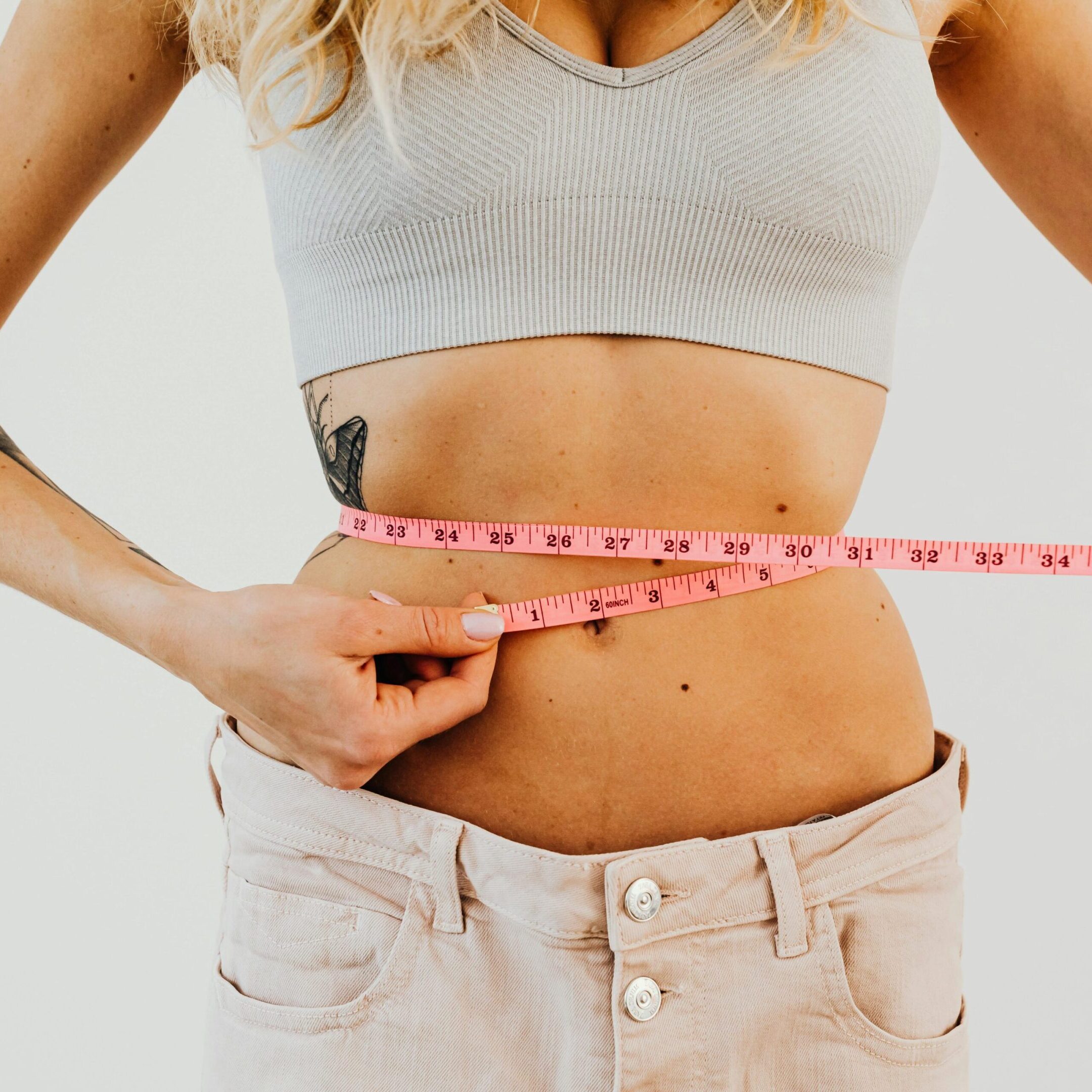 Woman measuring her waist with a pink tape measure.